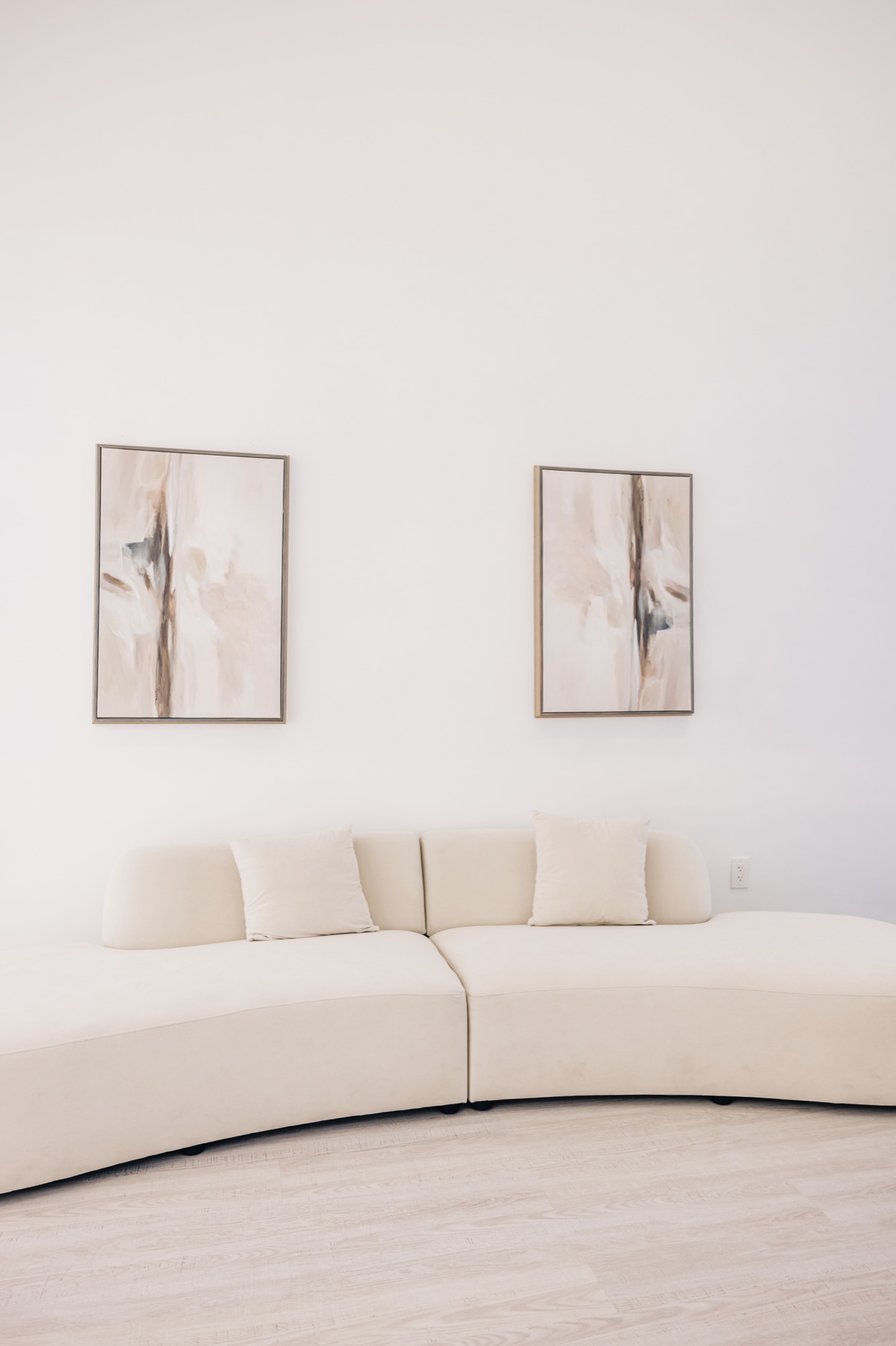 Curved cream sofa against a white wall with a pair of framed prints above it