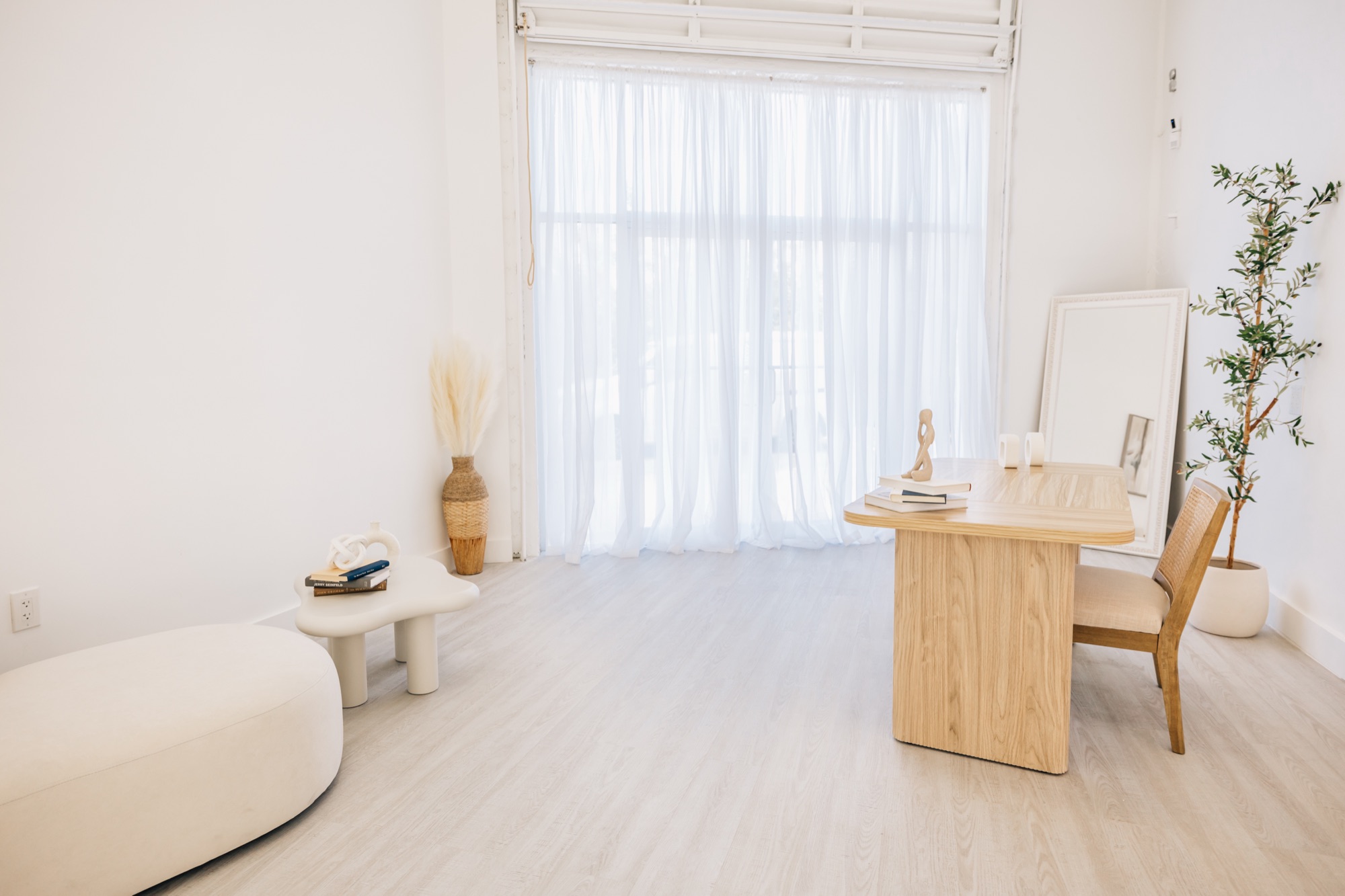Corner with a white ottoman, chair, and side table by the sheer curtains
